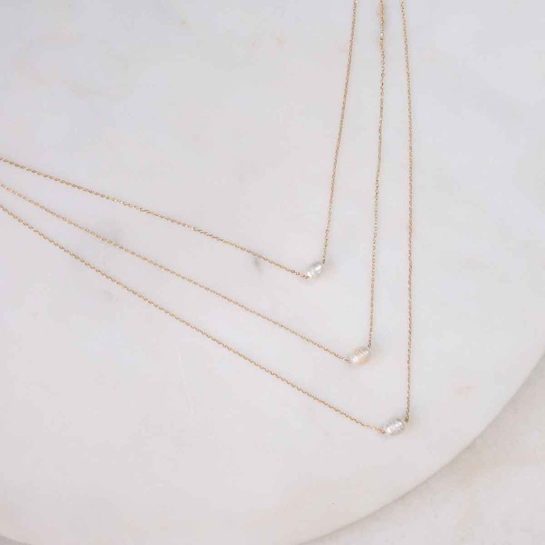 Enhance your style effortlessly with this triple-strand pearl necklace resting on a marble surface, offering a chic layered appearance in a single piece.