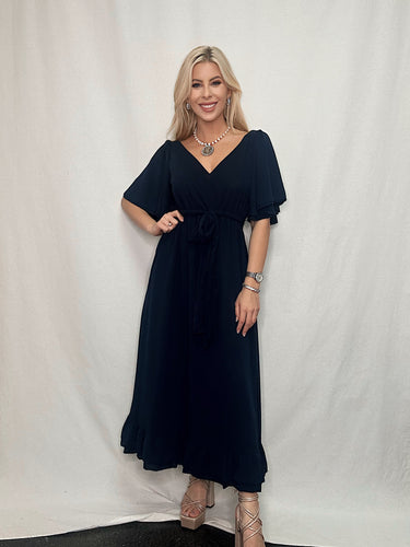 The model looks stunning in a navy dress with a v-neckline and ruffled sleeves. Perfect for any occasion, this Gretchen Scott dress will make you feel as fabulous as you look!