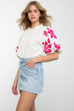 Load image into Gallery viewer, A model wearing a white blouse with pink floral patterns, showcasing the Alice Corduroy Top&#39;s cozy comfort and stylish embroidery.
